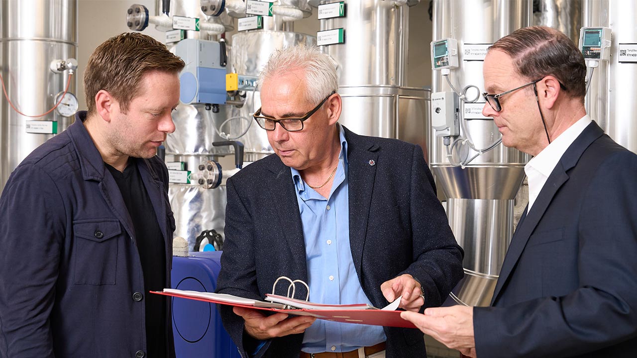 Drei Mitarbeitende von IBS und IWB stehen vor der neuen Heizzentrale