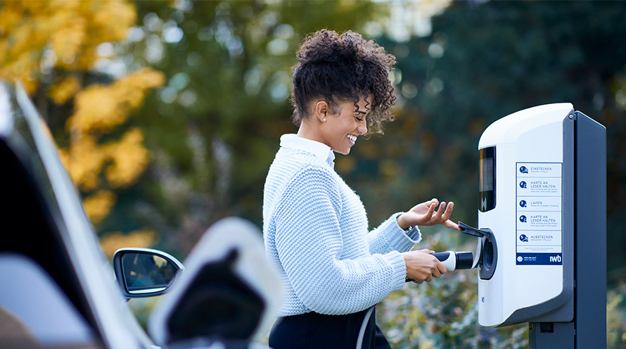 Mitarbeiterin lädt ihr Elektroauto auf dem Parkplatz ihres Unternehmens.