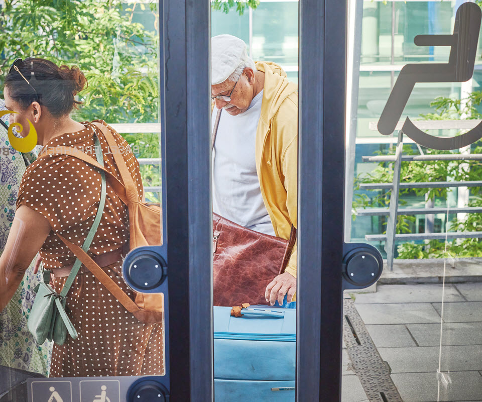 Touristen mit Koffern vor der Tür eines E-Busses.