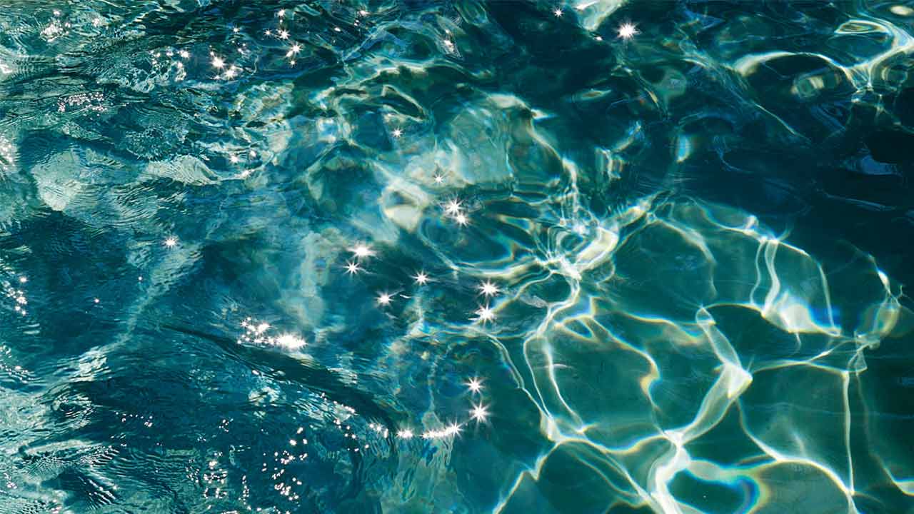 Wasserfläche von oben. Im Wasser spiegeln sich Sonnenstrahlen