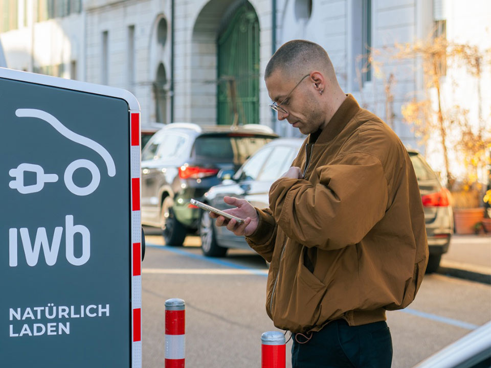 Mann steht mit Handy vor der öffentlichen IWB Ladestation