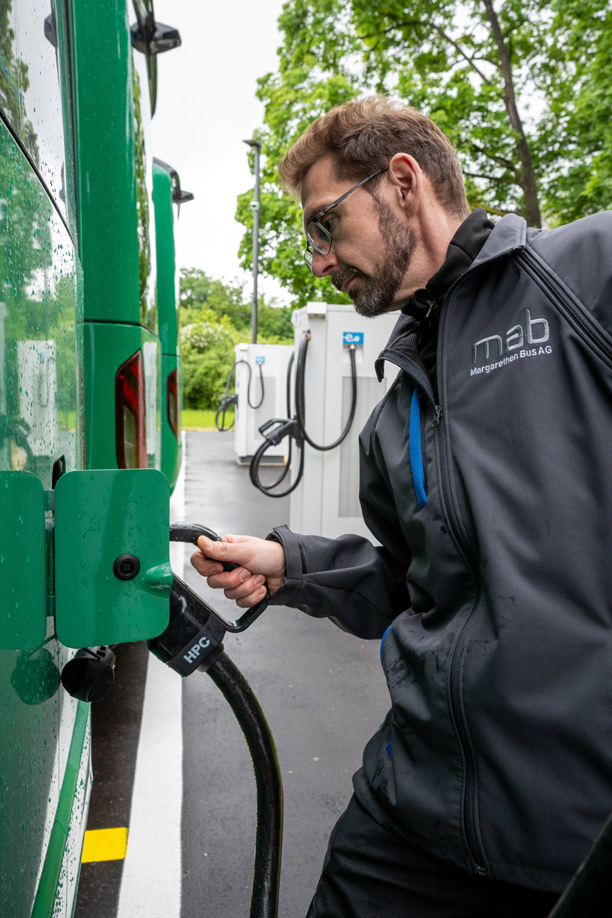 Fahrdienstleiter Benjamin Bossert an der Ladebuchse eines Busses. Die Stecker gleichen denen am E-Auto.