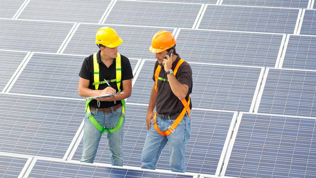 Zwei Arbeiter eines KMU mit Schutzausrüstung stehen zwischen Solarpanels.