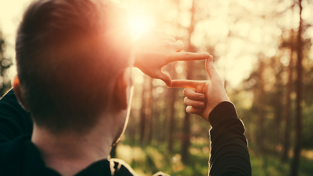 Mann im Wald misst symbolisch mit Fingern aus, wie gross seine Solaranlage sein muss.