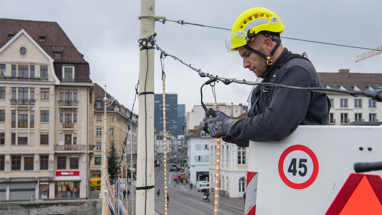 IWB Mitarbeiter befestigt Weihnachtsbeleuchtung an Brücke