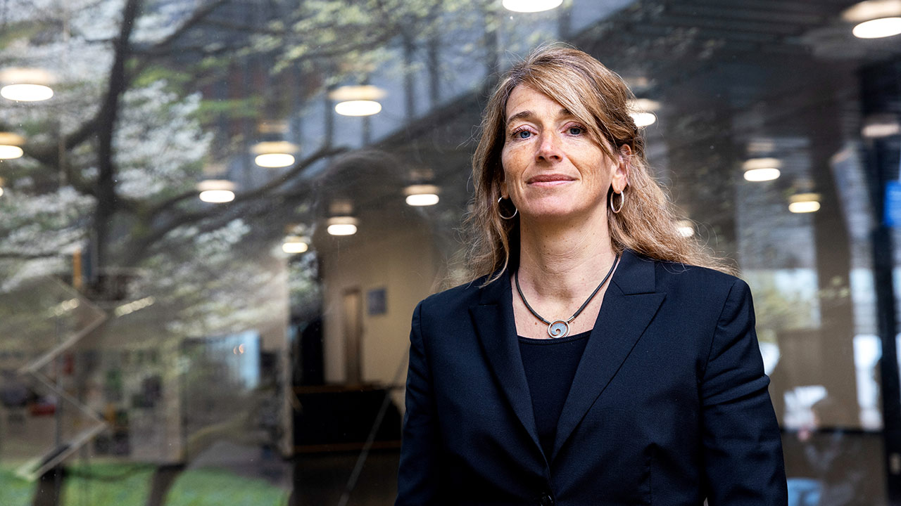 Prof. Dr. Adrienne Grêt-Regamey hinter einer Glasscheibe, im Hintergrund sind verschwommen Solarpanels zu sehen.